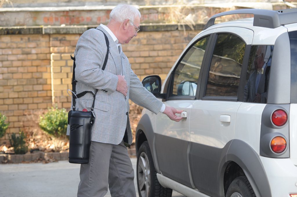 Ein Mann öffnet die Autotür. Er trägt den Spirit 1200 über der Schulter. tragbare Flüssigsauerstoffgeräte