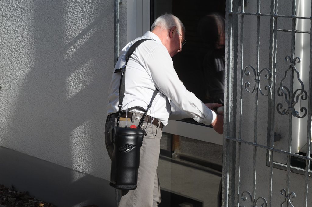 Ein Mann öffnet die Eingangstür. Er trägt den Spirit 1200 auf der Schulter. tragbare Flüssigsauerstoffgeräte